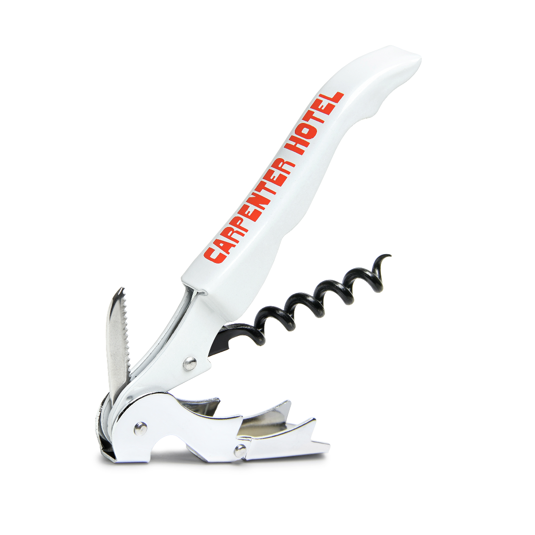 An open silver metal wine key with the Carpenter Hotel logo printed in orange-red on its side.