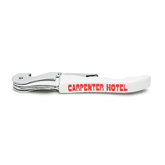 A silver metal wine key with the Carpenter Hotel logo printed in orange-red on its side.