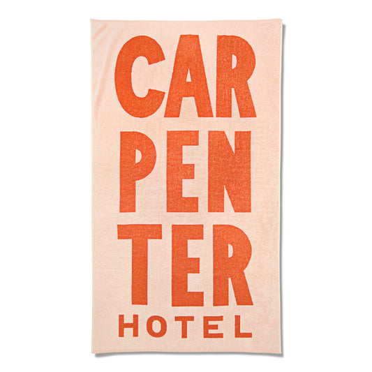 Light pink and orange pool towel that reads 'CARPENTER HOTEL' in large graphic letters