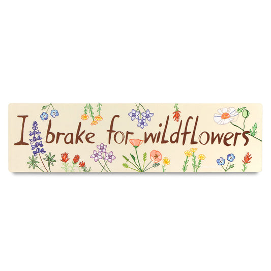 A bumper sticker with the phrase 'I brake for wildflowers' printed in a handwritten font, surrounded by an illustration of various wildflowers.