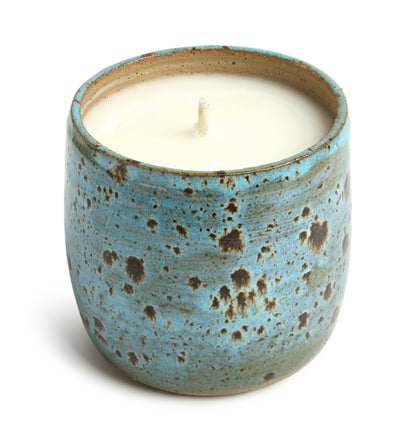 A ceramic candle vessel with a blue and brown speckled design with a candle wax insert.