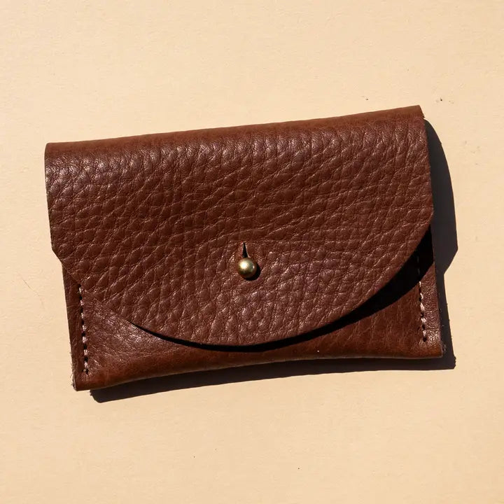 Pebbled leather chocolate brown cardholder with golden colored brass hardware against light yellow background