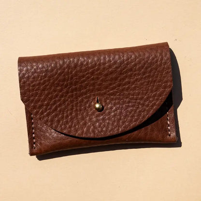 Pebbled leather chocolate brown cardholder with golden colored brass hardware against light yellow background