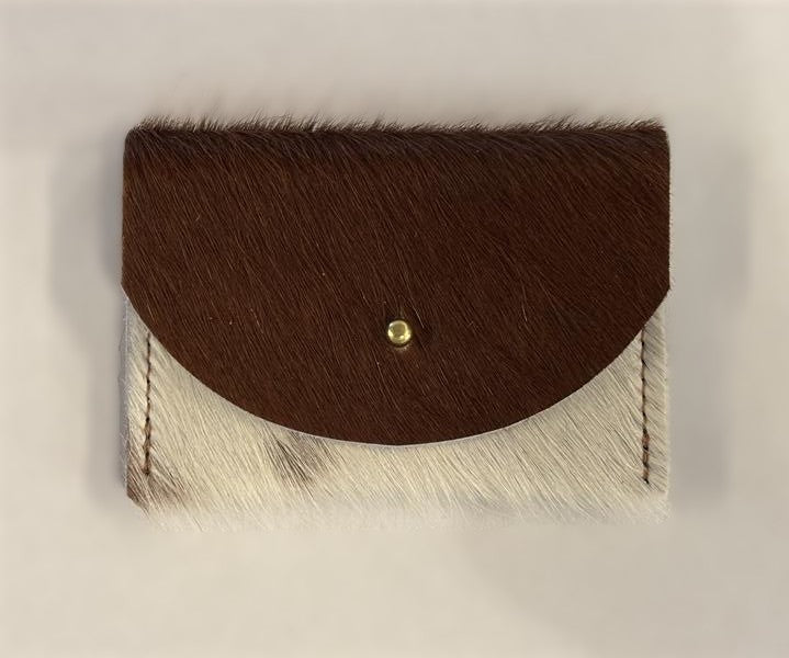 Brown and white cowhide cardholder with golden colored brass hardware against white background