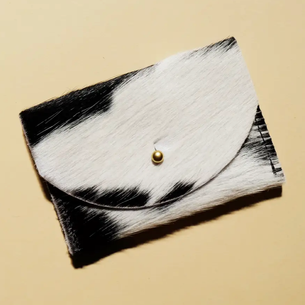 A black and white cowhide leather cardholder with a solid brass fastener, displayed against a neutral background.