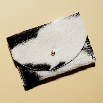 A black and white cowhide leather cardholder with a solid brass fastener, displayed against a neutral background.
