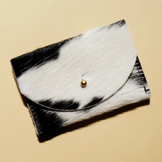 A black and white cowhide leather cardholder with a solid brass fastener, displayed against a neutral background.