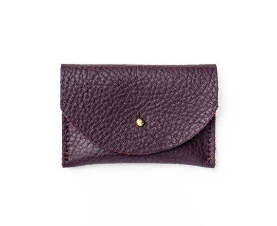 Pebbled leather plum purple cardholder with golden colored brass hardware against white background