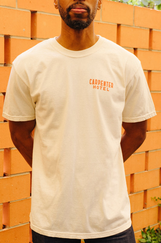Person wearing beige tshirt with text 'CARPENTER HOTEL' on left side of chest, standing in front of a terracotta wall.